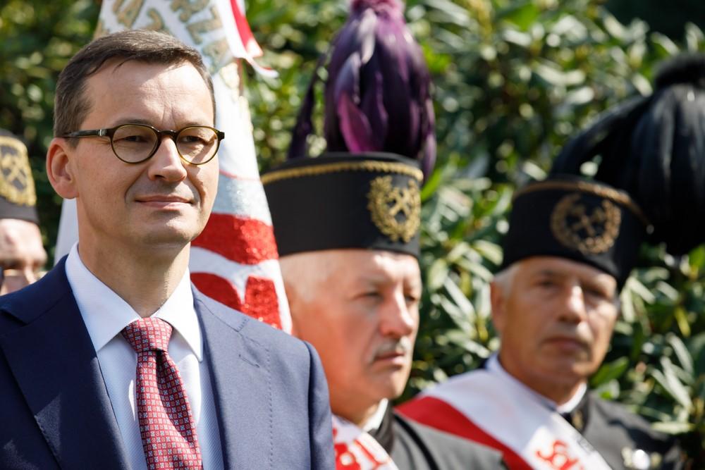 Premier Mateusz Morawiecki stoi a w tle górnicy.