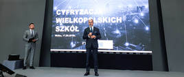 Minister Jerzy Kwieciński przemawia do publiczności. W tle prezentacja multimedialna