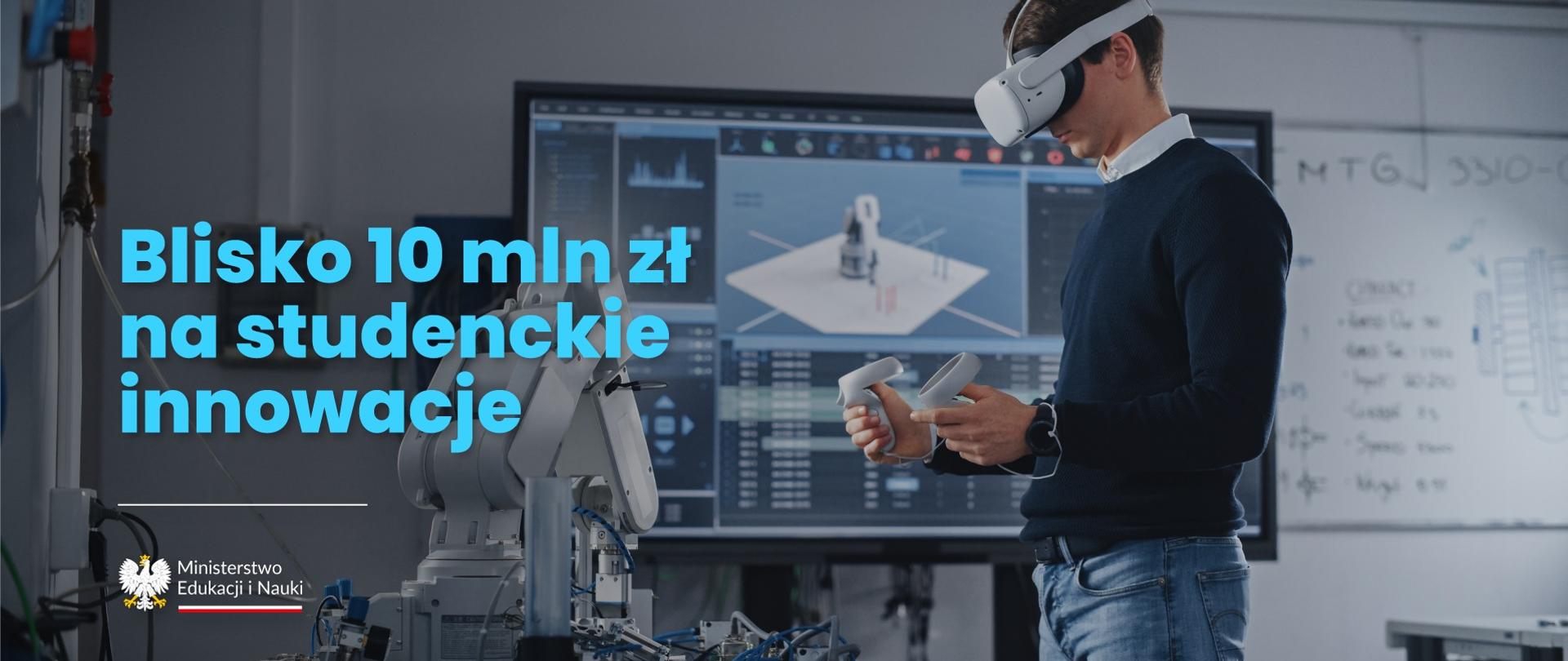 Przy stole na którym stoi ramię robota stoi młody człowiek w granatowym swetrze i w goglach wirtualnej rzeczywistości na głowie, za nim wielki monitor wyświetlający rysunek techniczny, obok niebieski napis Blisko 10 mln zł na studenckie innowacje.