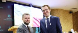 Dwie osoby stoją uśmiechnięte obok siebie i ściskają sobie dłonie. Pierwszy od prawej stoi wiceminister Jan Szyszko. 