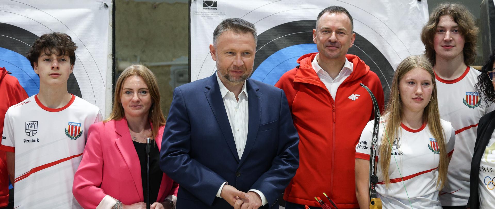 Briefing prasowy w Prudniku z okazji przekazania 42,3 mln zł do województwa opolskiego na odbudowę obiektów sportowych. Na pierwszym planie uczestnicy briefingu, na środku, w garniturze, Marcin Kierwiński, Minister ds. Odbudowy po Powodzi oraz Piotr Borys, Wiceminister Sportu i Turystyki (w czerwonej bluzie).