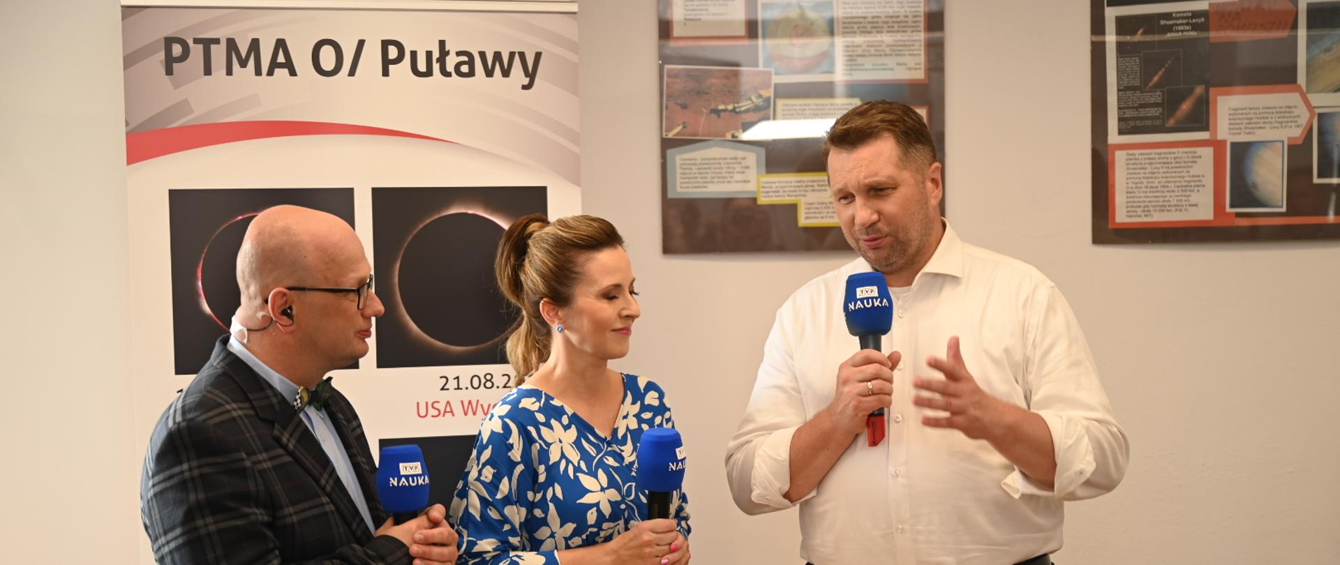 Dwóch mężczyzn i kobieta stoi z mikrofonami TVP i rozmawia.