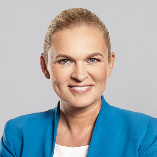 Minister Barbara Nowacka w niebieskiej marynarce na jasnoszarym tle.