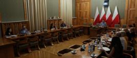 Ludzie siedzący przy stołach w dużej sali. W centrum wiceminister edukacji i nauki Dariusz Piontkowski na tle flag Polski