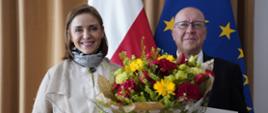 Wiceminister Joanna Mucha stoi obok nowego dyrektora ORPEG Adama Kalbarczyka, dyrektor trzyma w ręku akt powołania i bukiet kwiatów. W tle flagi Polski i UE. 