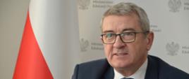 Wiceminister Murdzek siedzi przy biurku, za nim polska flaga.