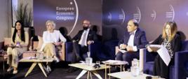 Na tle brązowej ściany z napisem European Economic Congress stoi pięć foteli, na nich siedzą trzy kobiety i dwóch mężczyzn, przed nimi trzy małe stoliki.