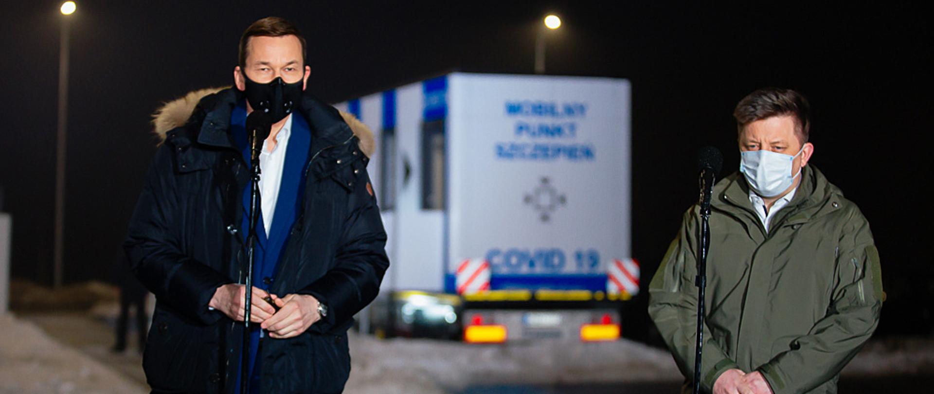Premier Mateusz Morawiecki i Michał Dworczyk stoją podczas briefingu.