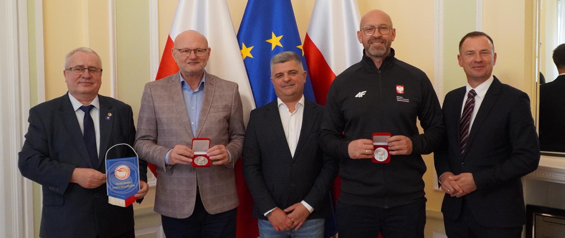 Zdjęcie zbiorowe. Od lewej stoją: sekretarz generalny Polskiego Związku Niesłyszących Jarosław Janiec, podsekretarz stanu w MSiT Ireneusz Nalazek, prezes związku Wojciech Stempurski, minister sportu i turystyki Jakub Rutnicki, sekretarz stanu w MSiT Piotr Borys. Z tyły flagi Polski i UE.