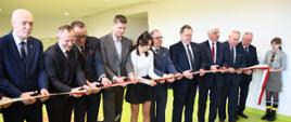 Mężczyźni w garniturach wraz z uczennicą przecinają wstęgę, którą trzyma harcerka