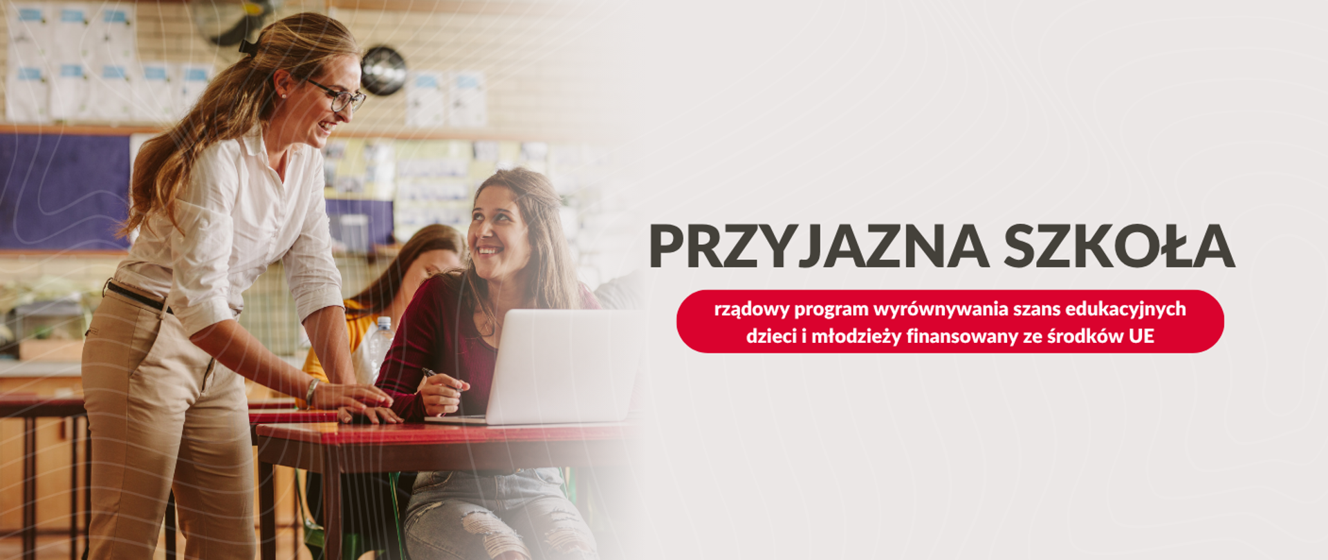 Grafika przedstawia uśmiechniętą nauczycielkę w okularach, pochylającą się nad uczennicą siedzącą przy biurku z laptopem. W tle widoczne są szafki. Po prawej stronie, na białym tle, znajduje się napis „PRZYJAZNA SZKOŁA” oraz czerwona belka z tekstem „rządowy program wyrównywania szans edukacyjnych dzieci i młodzieży finansowany ze środków UE”.
