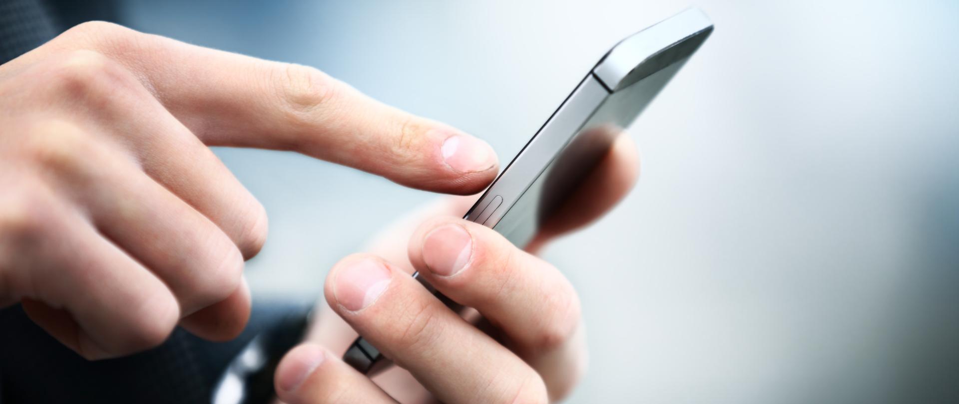 Osoba trzyma w ręku smartfon i coś na nim sprawdza