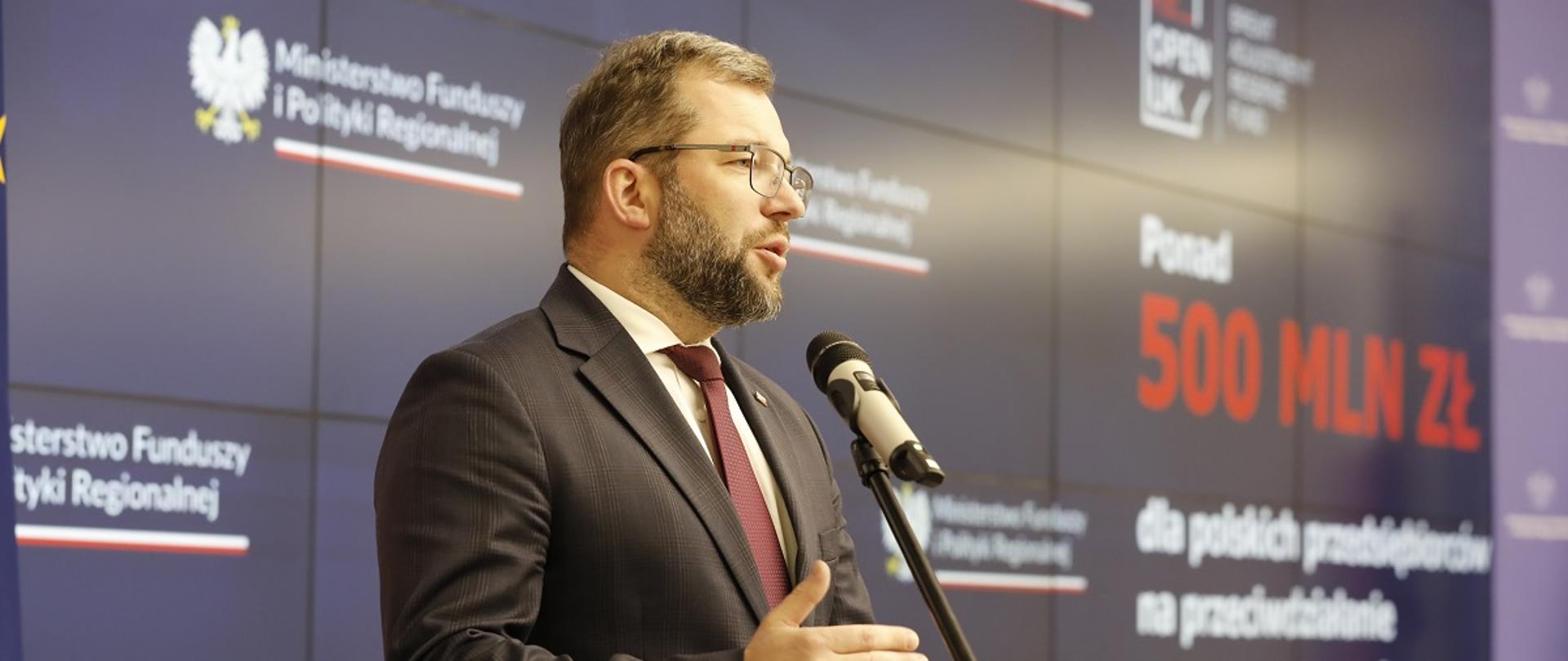 Minister funduszy i polityki regionalnej Grzegorz Puda stoi przy mikrofonie i przemawia, za jego plecami baner MFiPR z napisem o wsparciu 500 mln zł dla przedsiębiorców