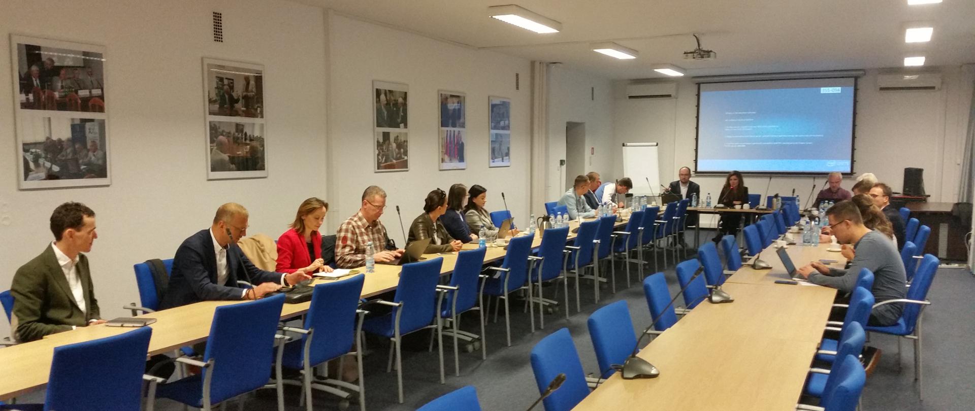 I posiedzenie Grupy Roboczej ds. Rozwoju Telekomunikacji. Ludzie siedzą przy stołach. W tle prezentacja multimedialna.