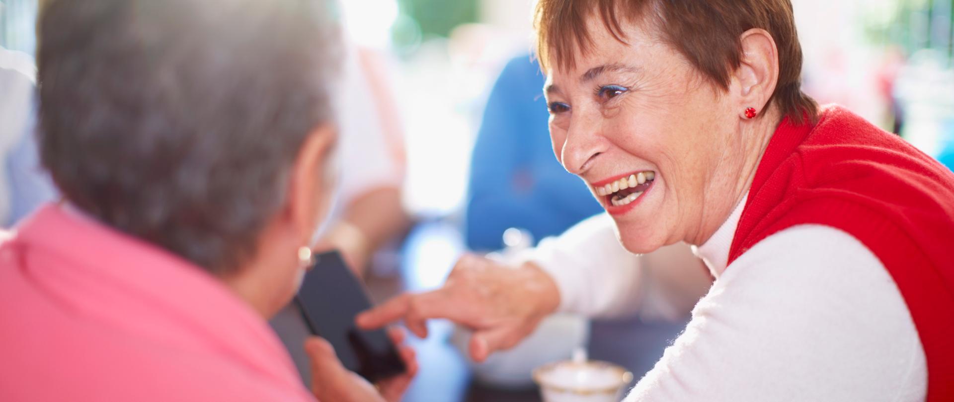 Happy senior woman showing smart phone to friend
