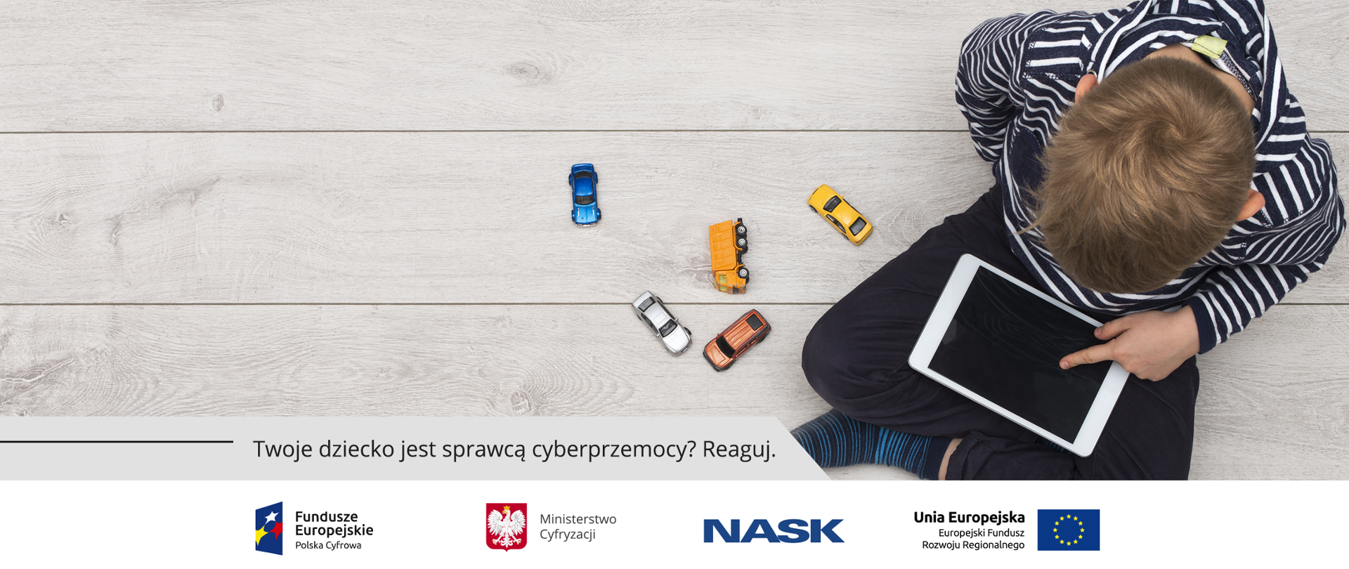 Chłopiec bawi się tabletem. Obok niego małe, zabawkowe samochodziki