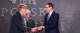 Premier ściska dłoń odznaczonego medalem mężczyzny.