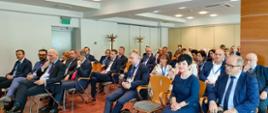 Sala konferencyjna. Grupa osób, w większości mężczyzn w garniturach. W pierwszym rzędzie wiceminister Bernacki. 