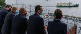Widok z tyłu na stojącego premiera z samorzadowcami i jezioro.
