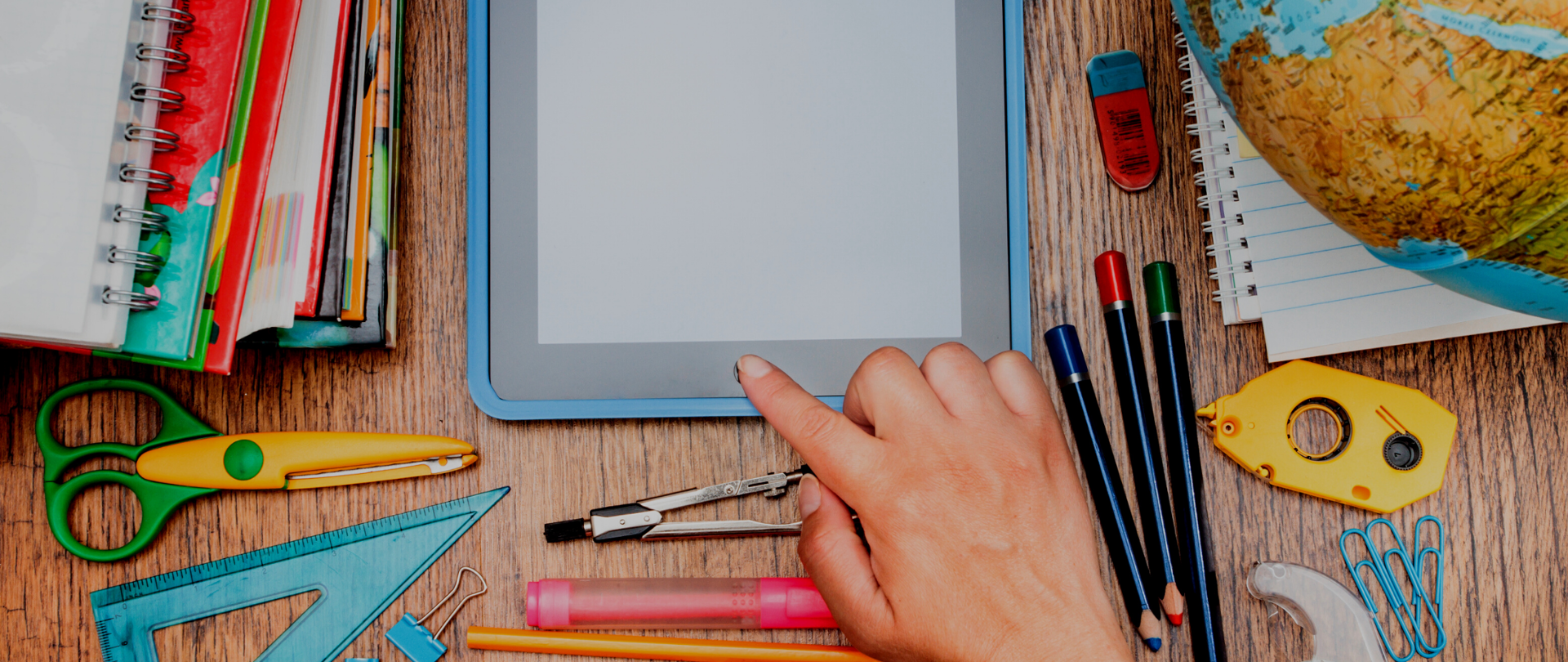 palec ludzki, który dotyka tablet, dookoła znajduje się dużo kolorowych, analogowych przyrządów do nauki 