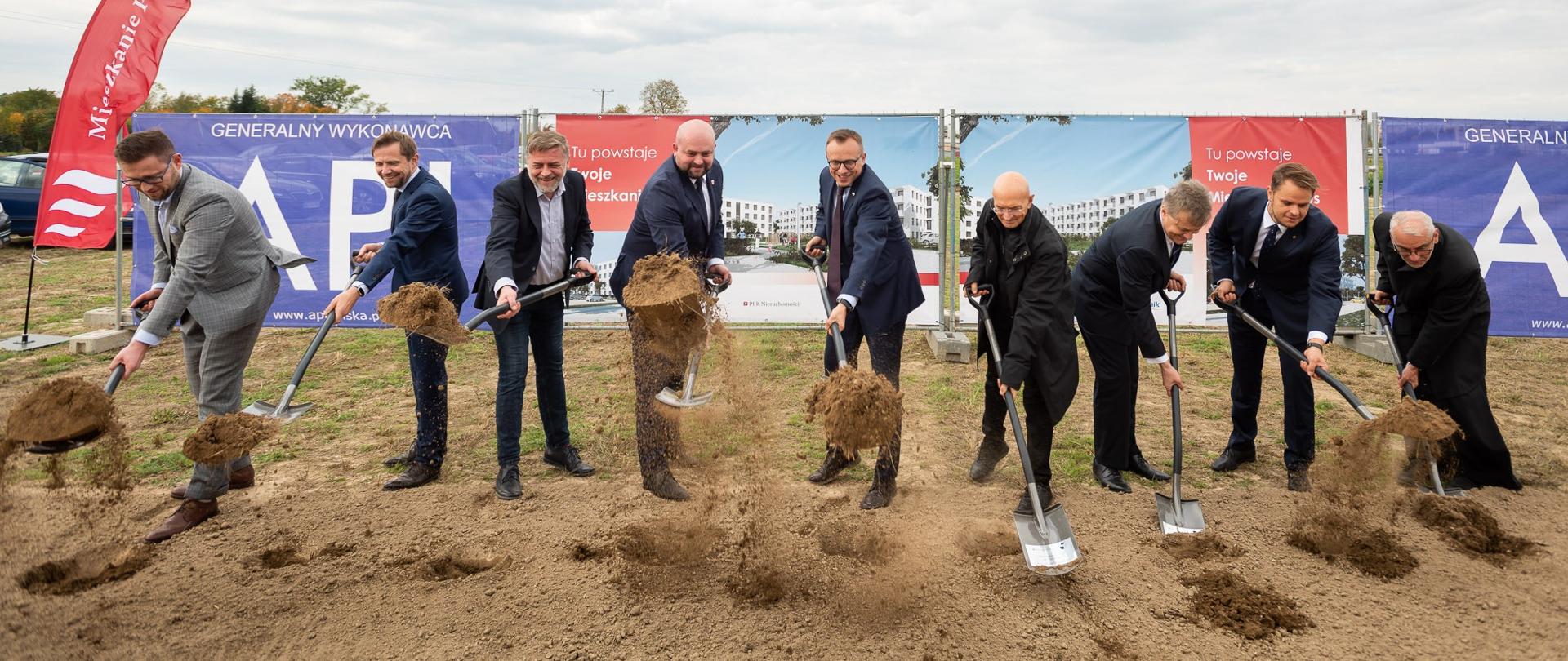 uczestnicy uroczystości wyrzucają w powietrze piasek z łopat wbitych symbolicznie