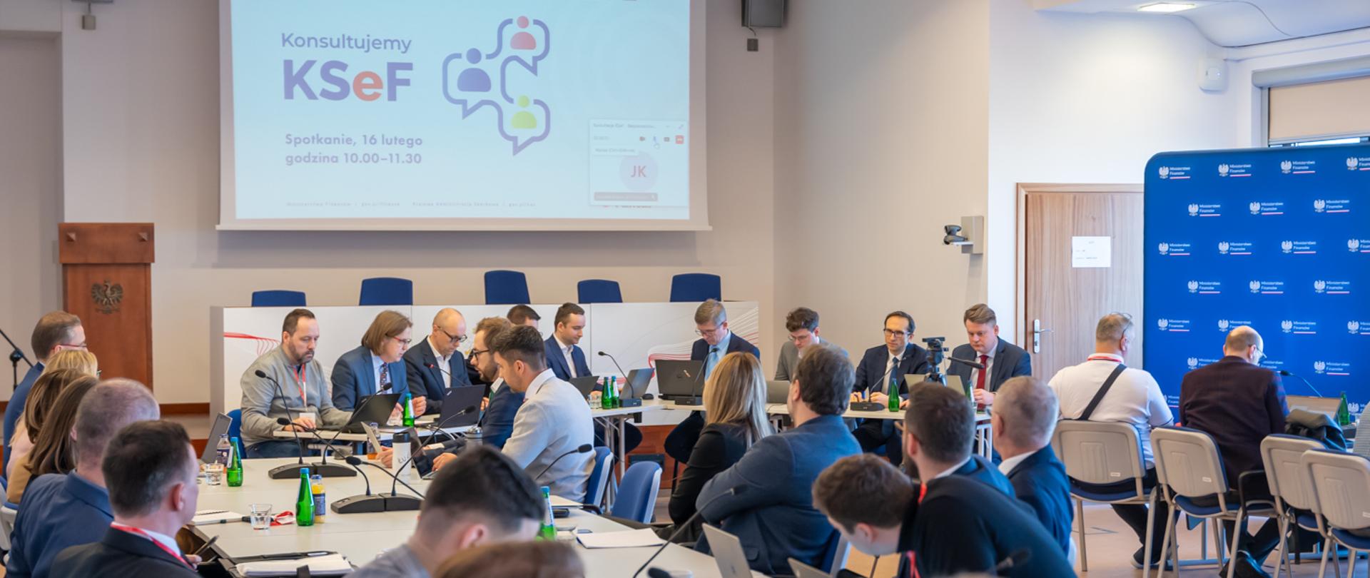 Kilkanaście osób siedzących przy stole podczas konsultacji