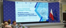 Posiedzenie Komitetu Koordynującego ds. Polityki Rozwoju, na ekranie grafika z napisem informującym o posiedzeniu KK ds. Polityki Rozwoju „Diagnoza systemu zarządzania rozwojem Polski – główne wnioski i rekomendacje” 