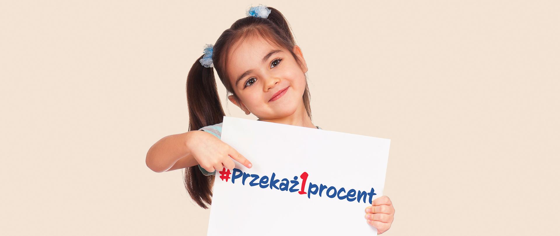 Uśmiechnięta dziewczynka z długimi włosami trzyma kartkę z napisem przekaż 1 procent 
