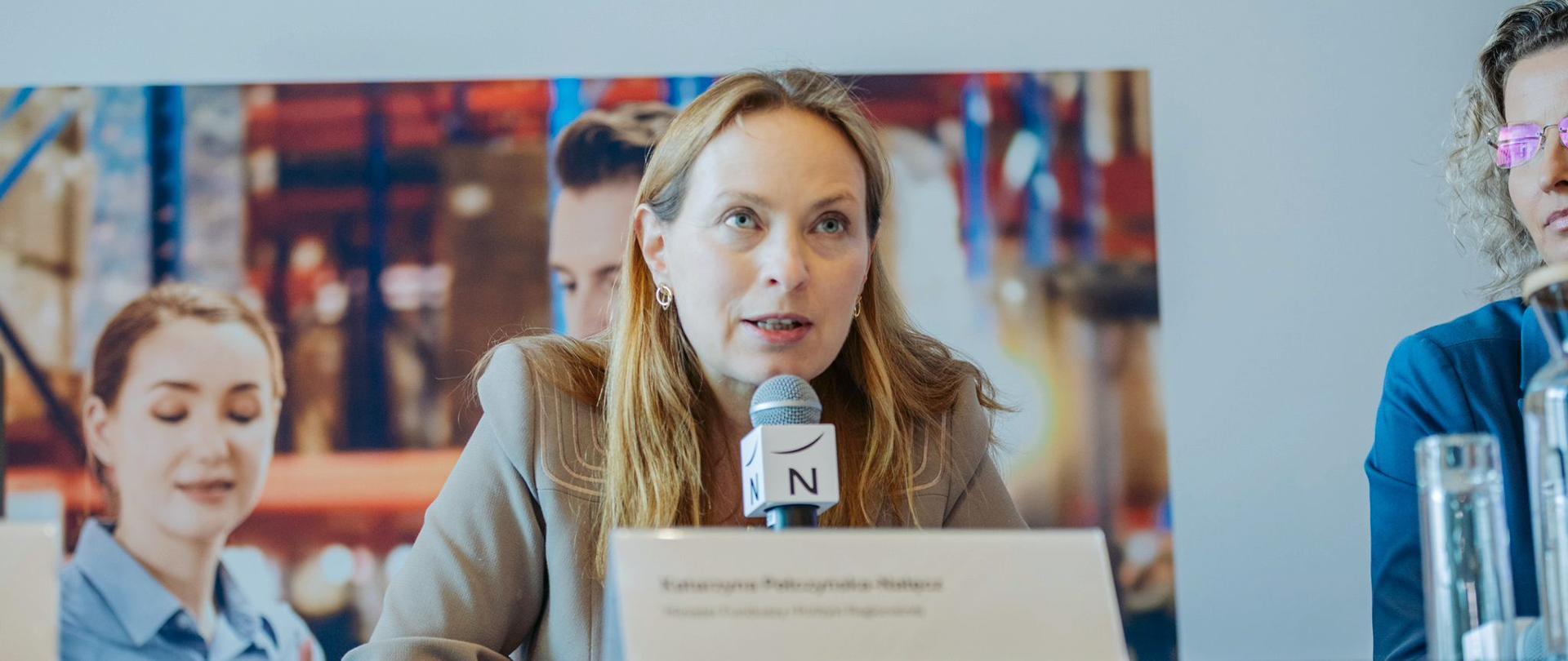 Minister Katarzyna Pełczyńska-Nałęcz z mikrofonem w ręku siedzi przy stole