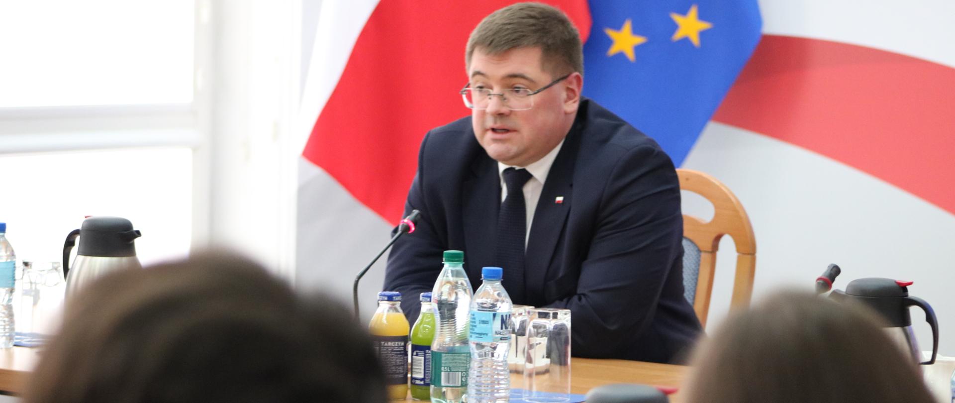 Wiceminister Tomasz Rzymkowski siedzi przy stole, przed nim siedzą uczniowie.