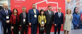 Na tle czerwonej ścianki z napisem NAWA - Ready Study Go! stoi grupa kilku osób.