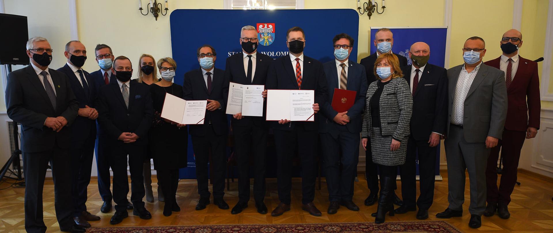 Podpisanie listu intencyjnego dotyczącego powstania Barki Edukacyjnej z udziałem ministra Przemysława Czarnka, minister Przemysław Czarnek stoi w towarzystwie sygnatariuszy porozumienia. W rękach trzymają dokument porozumienia.