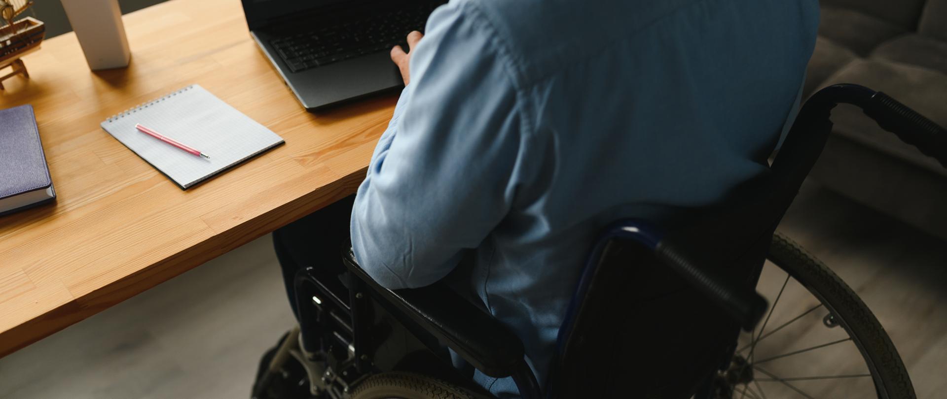 Young man with special needs in casual clothes working on wireless laptop. Male freelancer working from home while sitting in wheelchair