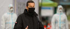 Premier stoi podczas przemówienia, w tle żołnierze WOT w kombinezonach.