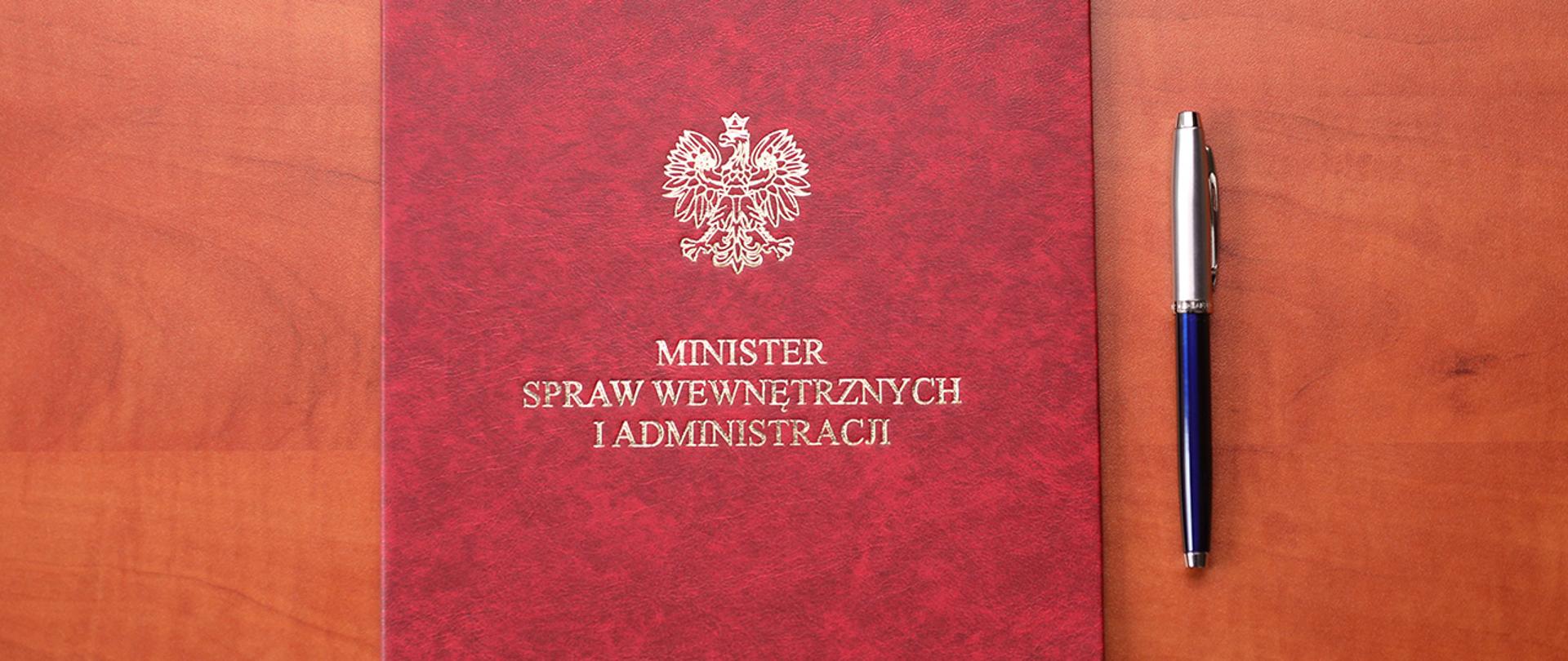 Teczka MSWiA z motywem orła z Godła RP oraz podpisem "Minister spraw wewnętrznych i administracji", obok leży długopis