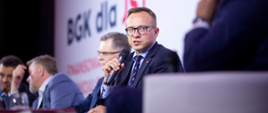 wiceminister Artur Soboń mówi do mikrofonu za nim widoczni inni uczestnicy debaty