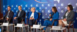 Wiceminister Machałek i cztery inne osoby - dwie kobiety i dwóch mężczyzn - siedzą na krzesłach, za nimi niebieska ściana.
