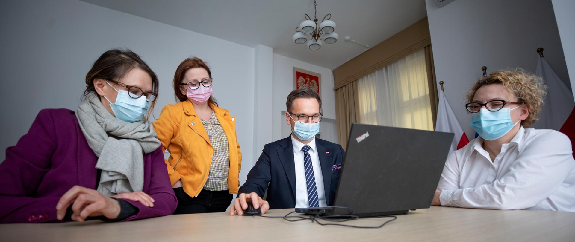 Cztery osoby siedzą przy stole wśród nich minister Buda, patrzą na komputer 