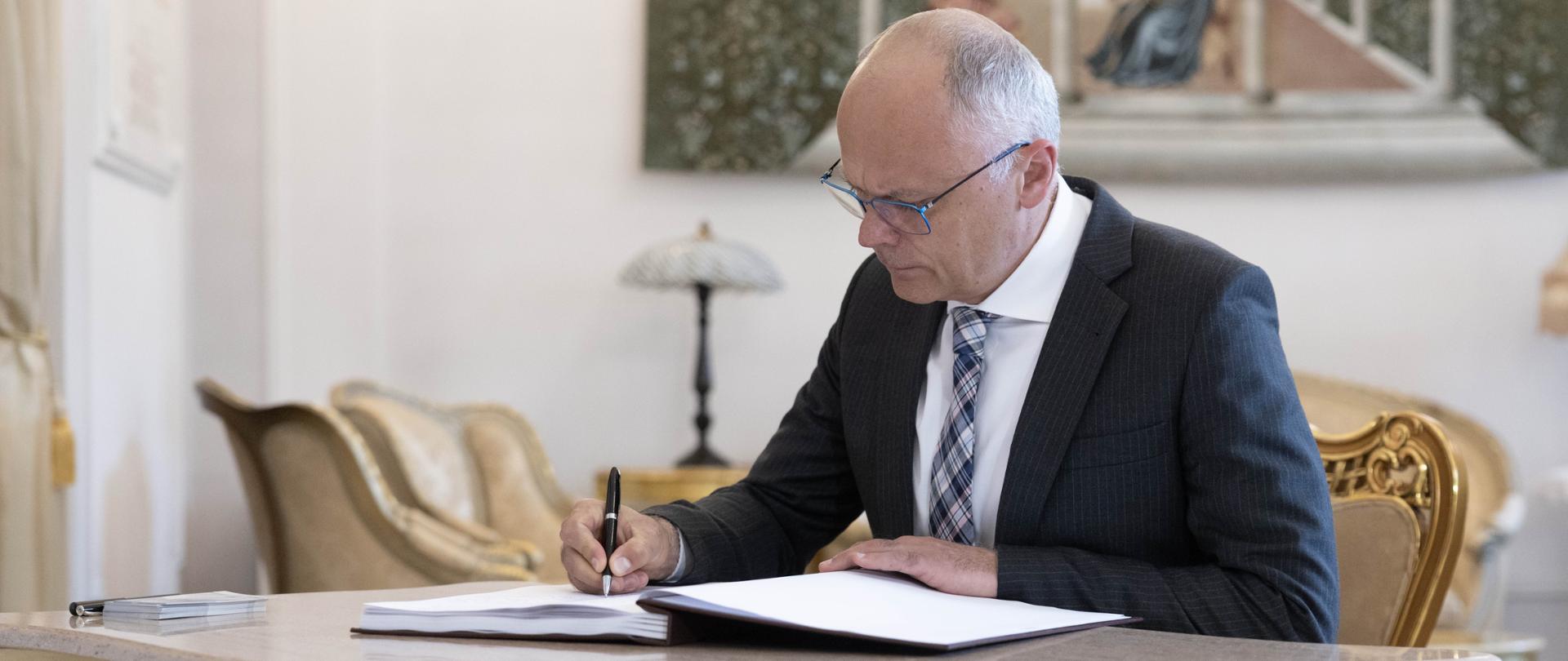 Minister Grzegorz Karpiński wpisuje się do księgi pamiątkowej.