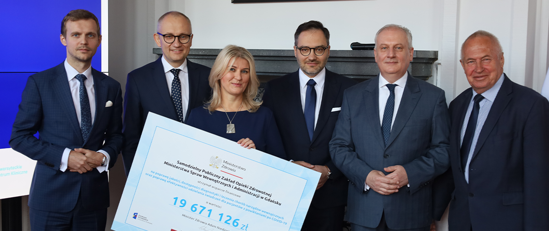 Wiceminister Błażej Poboży oraz inni zaproszeni goście pozujący do zdjęcia z czekiem przekazanym dla szpitala MSWiA w Gdańsku.