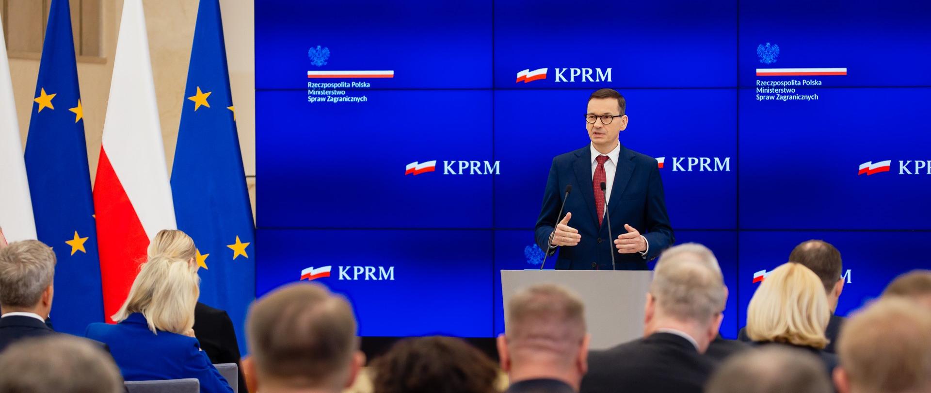 Premier Mateusz Morawiecki podczas spotkania z polskimi dyplomatami w ramach narady Ambasadorów RP.
Premier Mateusz Morawiecki stoi na tle ekranu, który wyświetla prezentacje. Szef rządu jest w trakcie wypowiedzi.