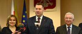 Szef MEiN mówi do mikrofonu. Po prawej i lewej stronie stoją mężczyzna i kobieta. 