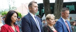 Minister Czarnek stoi na dworze, obok niego dwie kobiety i mężczyzna w garniturze, w tle widać żołnierzy.