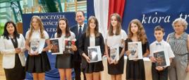 Osiem osób stoi w szeregu, trzymają książki, a nimi stoi wiceminister Bernacki.