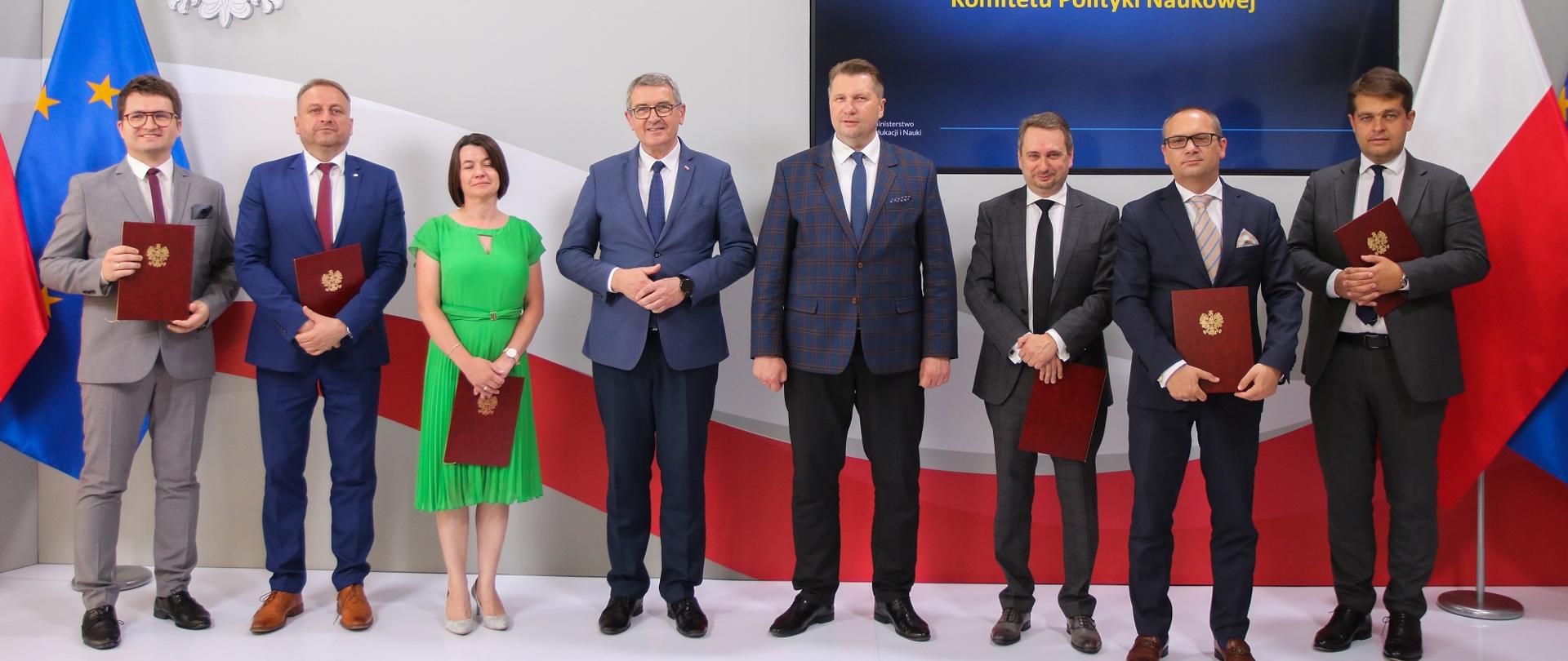 Zdjęcie zbiorowe uczestników uroczystości, stoją w rzędzie, za nimi wzór polskiej flagi i ekran z napisem Wręczenie powołań dla członków KPN.