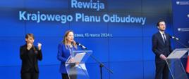 Minister funduszy i polityki regionalnej Katarzyna Pełczyńska-Nałęcz i wiceminister Jan Szyszko stoją przy pulpitach z mikrofonami, za nimi niebieska grafika z informacją o rewizji KPO
