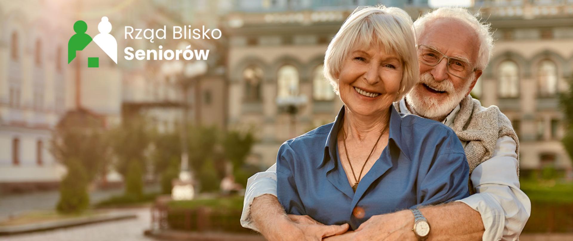 Na zdjęciu para seniorów przytulających się. W lewym górnym rogu logo programu Rząd Blisko Seniorów