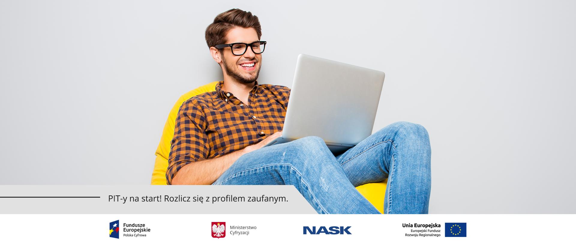 Mężczyzna w jeansach i pomarańczowo-granatowej koszuli w kratkę siedzi uśmiechnięty na dużym żółtym fotelu w kształcie worka. Na kolanach trzyma laptopa. Napis: PIT-y na star! Rozlicz się z profilem zaufanym. 