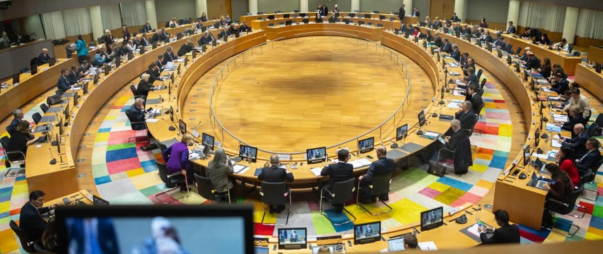 Sala podczas posiedzenia Rady UE ds. Wymiaru Sprawiedliwości i Spraw Wewnętrznych w Brukseli. Na pierwszym planie mały monitor wyświetlający jedną z osób obradujących, twarz jest rozmyta.