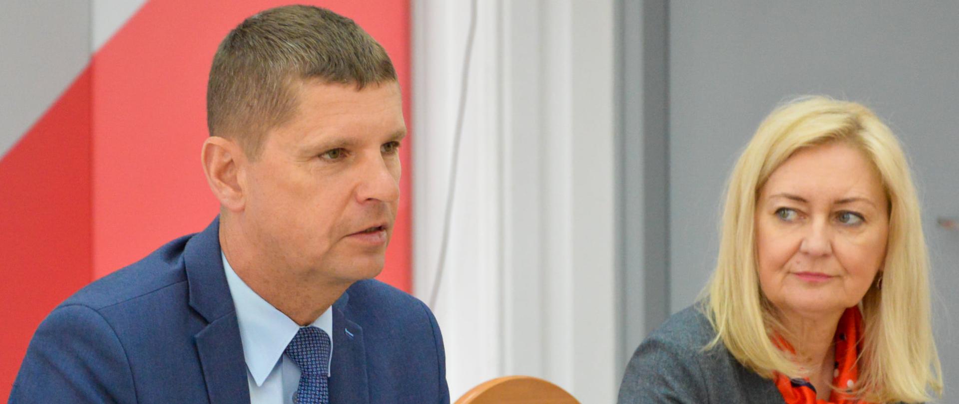 Wiceminister Dariusz Piontkowski oraz inna uczestniczka obrad podczas spotkania. Siedzą przy stole.